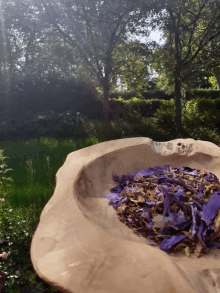 a wooden bowl filled with purple petals in front of trees