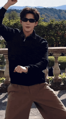 a man wearing sunglasses and a black sweater is standing in front of a fence