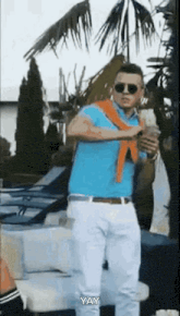 a man in a blue polo shirt and white pants is standing in front of a palm tree .