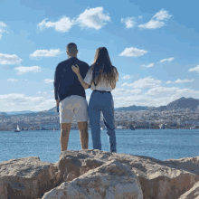 a man and a woman are standing on a rock overlooking the ocean