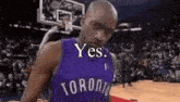 a man in a toronto raptors jersey is standing on a basketball court with a basketball hoop in the background .