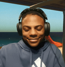 a man wearing headphones and a blue adidas sweatshirt smiles