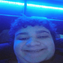 a person with curly hair is smiling in front of blue lights