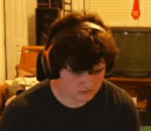 a young man wearing headphones and a black shirt is sitting in front of a television .