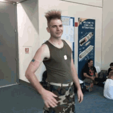 a man in a tank top and camo pants is standing in front of a welcome to comic con international sign