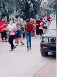 a group of people are walking down a street while a car is parked on the side of the road .