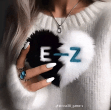 a woman is wearing a white sweater and holding a black and white heart with the letter e and z on it .