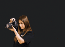 a man holds a camera in front of a girl who is wearing a black shirt that says ' do ' on the back