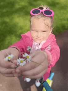 a little girl wearing pink sunglasses and a pink jacket is holding flowers