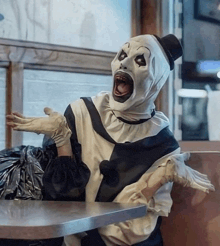 a clown is sitting at a table with his mouth wide open