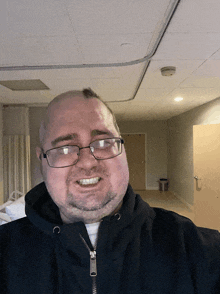 a man wearing glasses and a black jacket smiles in an empty room