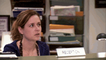 a woman sits at a reception desk with a name plate that says reception