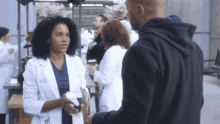 a woman in a lab coat talks to a man in a black hoodie