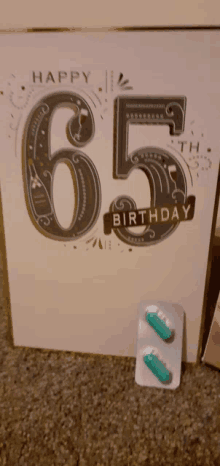 a happy 65th birthday card next to two pills