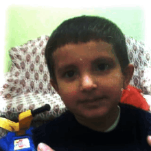 a young boy in a black shirt looks at the camera with a toy train in the background