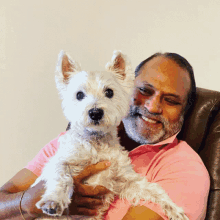 a man in a pink shirt holding a small white dog