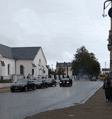 a row of black cars are parked on the side of a street in front of a white building with a sign that says sjukhus