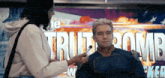 a woman brushes a man 's face in front of a sign that says truth bomb