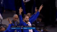 a man in a blue shirt is giving the ok sign while sitting in the stands during a basketball game