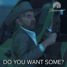 a man in a suit and cowboy hat is holding a gun and asking " do you want some "