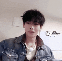 a young man wearing a denim jacket and a necklace is looking at the camera