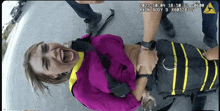 a woman in a purple shirt is laying on the ground with her mouth open while being held by a police officer