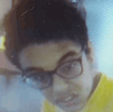 a man wearing glasses and a yellow shirt is looking at a computer screen .