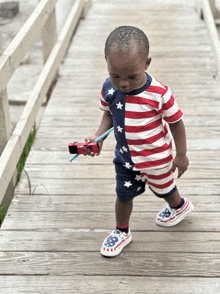 a little boy wearing an american flag outfit holds a red toy car