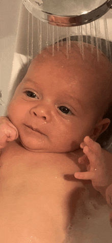 a baby is taking a shower in a bathtub and looking at the camera