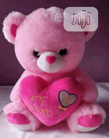 a pink teddy bear is sitting on a bed holding a pink heart shaped pillow .