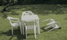 a set of white plastic chairs and a table on a lush green lawn