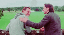 two men are hugging each other and laughing in front of a field