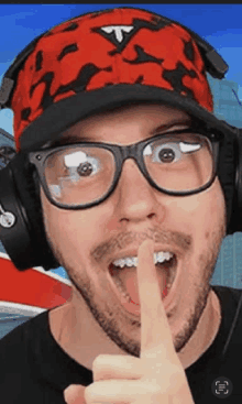 a man wearing glasses and headphones has his finger on his mouth