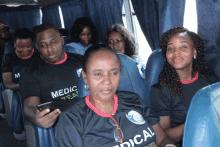 a group of people are sitting on a bus wearing black shirts that say medic tea