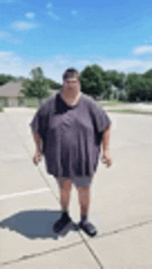 a very fat man is standing on a sidewalk wearing shorts and a t-shirt .