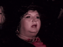 a woman wearing a wig and earrings is making a funny face while sitting in a dark room .
