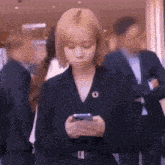 a woman in a suit is looking at her cell phone while standing in a crowd of people .