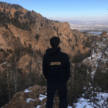 a man in a black johnson hoodie stands on top of a snowy mountain