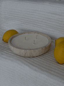 a round candle with three candles in it sits on a table next to lemons