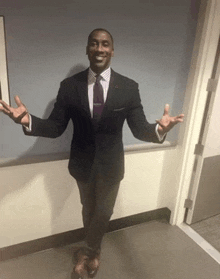 a man in a suit and tie stands in a hallway with his arms outstretched