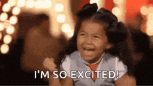 a little girl is laughing and saying `` i 'm so excited '' while holding her fist in the air .