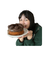 a woman in a green sweatshirt is eating a cake with chocolate frosting