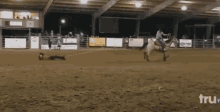 a man is laying on the ground in a rodeo arena while a man rides a horse in the background