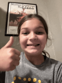 a young girl is giving a thumbs up in front of a framed poster for western trappings the llano