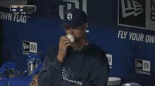 a man wearing a san diego padres hat holds a baseball in front of a sign that says fly your own flag