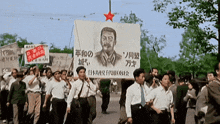 a group of people marching down a street holding a banner with a picture of a man with a mustache on it