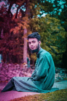 a young man with a beard is sitting on a rock in the grass