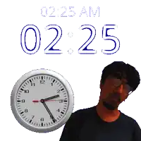 a man stands in front of a wall clock that says 0225 am