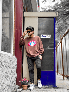 a man leans against a wall in front of a pay24 box