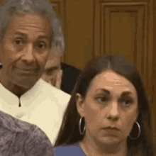 a man and a woman are sitting next to each other in a courtroom . the woman is wearing hoop earrings .